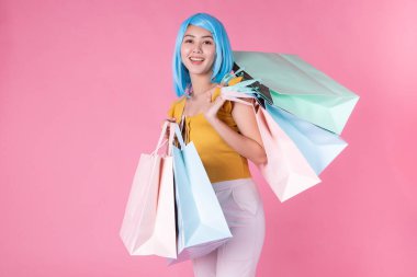 Renkli alışveriş çantalarıyla oldukça heyecanlı Asyalı bir kızın portresi pembe arka planda soyutlanmış görünüyor. Alışveriş torbaları taşıyan alışveriş kolik bir kadın yaz indirimi konsepti için. Genç mavi saçlı kız. .