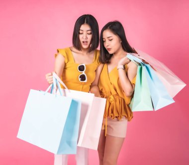 Pembe pastel arka planda oturan Asyalı güzel genç bayan. Gülümsüyor ve alışveriş torbaları ile mutlu. Hoş görünümlü, çekici, parlak. Arkadaşı alışveriş zamanından memnun..