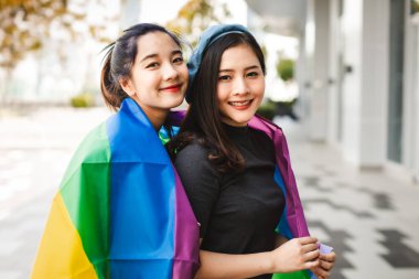 Lezbiyen çift portresi, gökkuşağı bezinin altında dudaklarını öpen Asyalı kadın portresi, lezbiyen kavramları. Farklı ırktan iki güzel kadın gökkuşağı bayrağına sarılarak oynuyorlar.