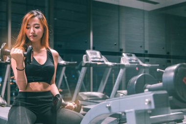 Güzel vücutlu, kaslı, genç Asyalı kadın halterle egzersiz yapıyor. Sportif kız spor salonunda ağırlık kaldırıyor..
