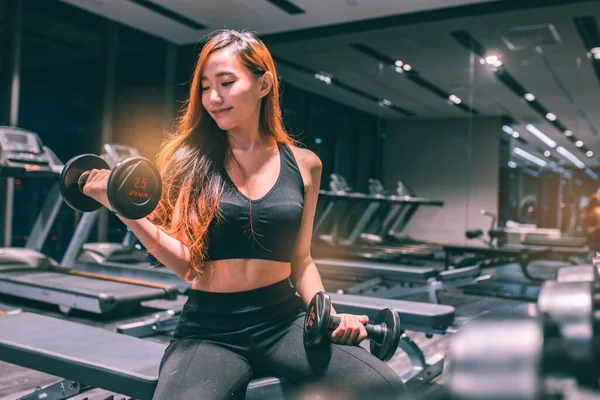 Güzel vücutlu, kaslı, genç Asyalı kadın halterle egzersiz yapıyor. Sportif kız spor salonunda ağırlık kaldırıyor..