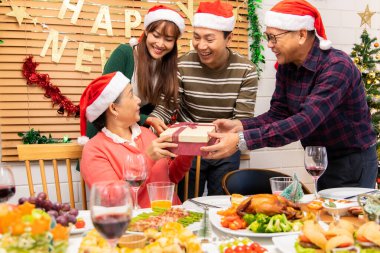 Şükran Günü ya da Noel Kutlaması Asya Aile Yemeği Konsepti. Mutlu bir aile Noel 'i büyükannesi ve büyükbabasıyla kutlarken bir yandan da Noel Baba şapkası ve hediye kutusu takıyor..