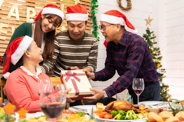 Şükran Günü ya da Noel Kutlaması Asya Aile Yemeği Konsepti. Mutlu bir aile Noel 'i büyükannesi ve büyükbabasıyla kutlarken bir yandan da Noel Baba şapkası ve hediye kutusu takıyor..