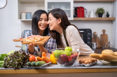LGBT Lezbiyen çifti evde sağlıklı sebze salatası pişirmeye bayılır. İki güzel bayan kız arkadaş mutfakta yemek pişirir, sarılır ve güler.