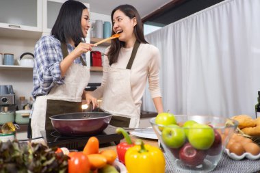 LGBT Lezbiyen çifti evde sağlıklı sebze salatası pişirmeye bayılır. İki güzel bayan kız arkadaş mutfakta yemek pişirir, sarılır ve güler.