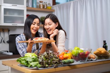 LGBT Lezbiyen çifti evde sağlıklı sebze salatası pişirmeye bayılır. İki güzel bayan kız arkadaş mutfakta yemek pişirir, sarılır ve güler.