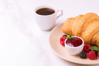 Bir fincan sıcak kahve, reçel ve meyveler kahvaltıda taze kruvasan. Seçici odak