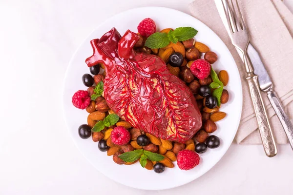 Healthy food and heart model on white plate. Nuts and berries. Medical abstract concept
