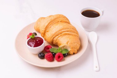 Bir fincan sıcak kahve, reçel ve meyveler kahvaltıda taze kruvasan. Seçici odak