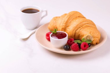 Bir fincan sıcak kahve, reçel ve meyveler kahvaltıda taze kruvasan. Seçici odak