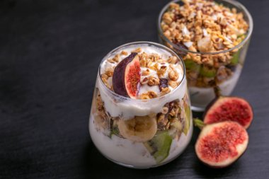 Yoğurt ve taze muz ve siyah arduvaz arka planda incir ile ev yapımı granola bardak. Yatay görünüm. Kopya alanı
