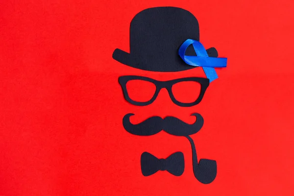 Male silhouette with mustache, glasses and hat patterns and blue ribbon symbol on the red background. Movember concept. Prostate Cancer and men's health awareness.