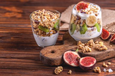 Yoğurt ve taze muz ve ahşap arka plan üzerinde incir ile ev yapımı granola bardak. Yatay görünüm. Kopya alanı