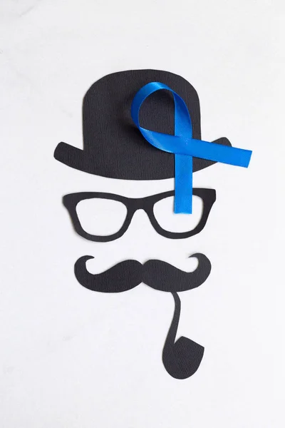 Male silhouette with mustache, glasses and hat patterns and blue ribbon symbol on the white background. November concept. Prostate Cancer and men's health awareness.
