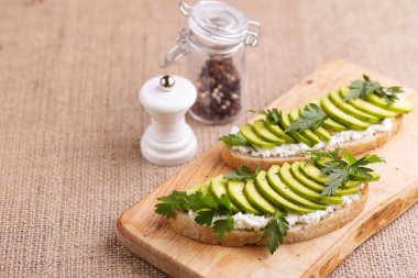 Avokado tost corn bread ile maydanoz, tuz ve biber için sağlıklı kahvaltı ya da çuval bezi arka plan üzerinde hafif öğle yemeği ile krem peynir. Vejetaryen yiyecekler. Yatay görünüm. Kopya alanı.