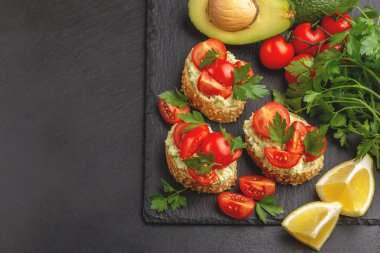 Bruschetta ile doğranmış domates, siyah arduvaz arka plan üstten görünüm üzerinde avokado ve taze maydanoz püresi. Kopya alanı