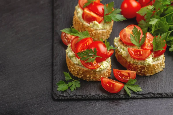 Bruschetta with chopped cherry tomatoes, puree avocado and fresh parsley on the black slate background Horizontal view. Copy space