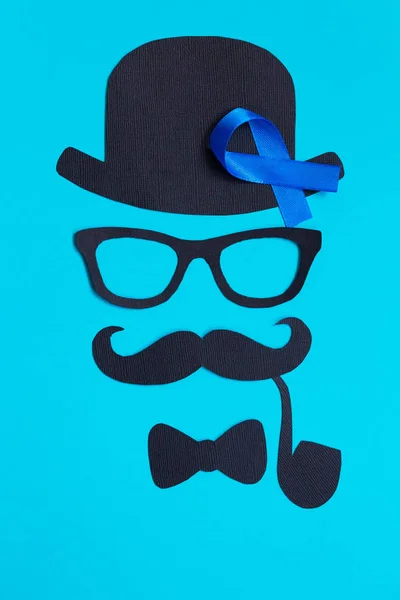 Male silhouette with mustache, glasses and hat patterns and blue ribbon symbol on the blue background. Movember concept. Prostate Cancer and men\'s health awareness.