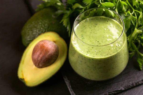Fresh spinach and avocado smoothie in glass with parsley on black slate background. Horizontal view. Copy space