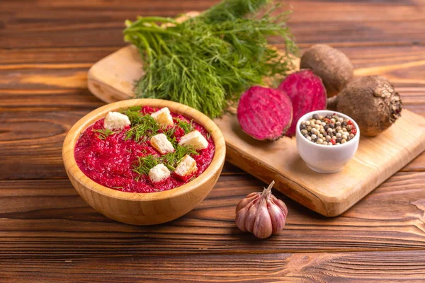 Bright lezzetli kırmızı pancar çorbası kesme tahtası üzerinde malzemelerle ahşap kase ezilmiş. Sağlıklı gıda kavramı. Rustik ahşap arka plan. Yatay görünüm. Kopya alanı