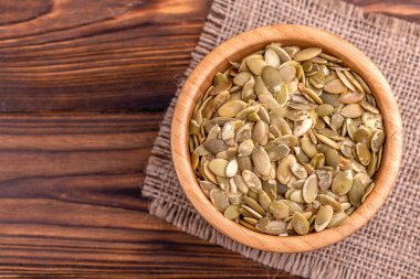 Çuval bezi peçete ahşap arka plan üzerinde ahşap kase taze kabak çekirdeği. Uzay kopyalayın. Üstten görünüm