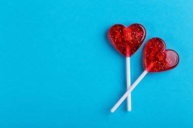 İki kırmızı tatlı lezzetli lolipop parlak mavi arka plan üzerinde kalp şeklinde. St. Valentine's day. Kopya alanı