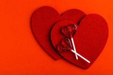 İki kırmızı tatlı lezzetli lolipop ve parlak kırmızı zemin üzerine iki keçe kalp. St. Valentine's day. Kopya alanı