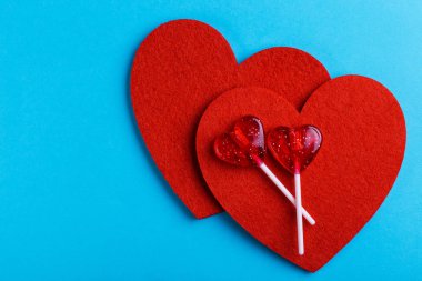 İki kırmızı tatlı lezzetli lolipop ve parlak mavi zemin üzerine iki keçe kalp. St. Valentine's day. Kopya alanı