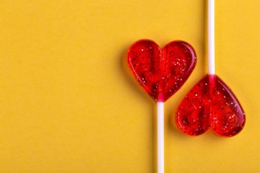 İki kırmızı tatlı lezzetli lolipop parlak sarı zemin üzerinde kalp şeklinde. St. Valentine's day. Kopya alanı
