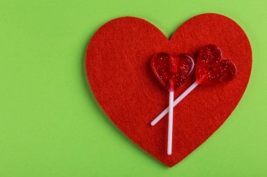 İki kırmızı tatlı lezzetli lolipop ve parlak yeşil zemin üzerine keçe kalp. St. Valentine's day. Kopya alanı