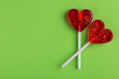 İki kırmızı tatlı lezzetli lolipop parlak yeşil arka plan üzerinde kalp şeklinde. St. Valentine's day. Kopya alanı