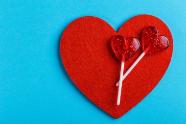 İki kırmızı tatlı lezzetli lolipop ve keçe kalp üzerinde parlak arka plan mavi. St. Valentine's day. Kopya alanı