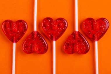 Beş kırmızı tatlı lezzetli lolipop parlak turuncu zemin üzerinde kalp şeklinde. St. Valentine's day. Kopya alanı