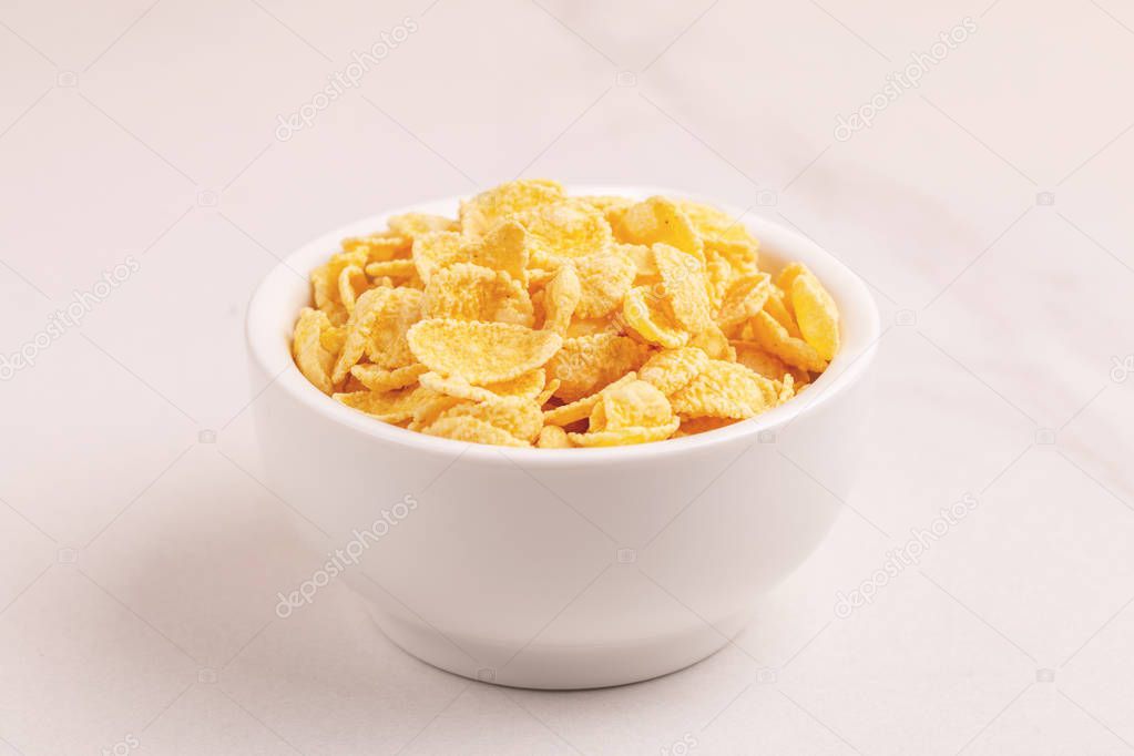 Crispy corn flakes in clay bowl on light marble background. Healthy cereals breakfast. Copy space