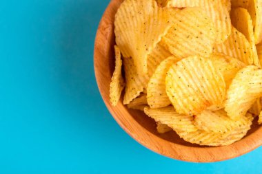 Çıtır patates cipsi ahşap kase parlak mavi zemin üzerine oluklu. Abur cubur. Kopya alanı