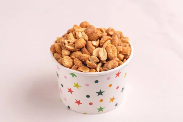 Roasted peanuts in paper cup on light marble background. Movie snacks. Copy space
