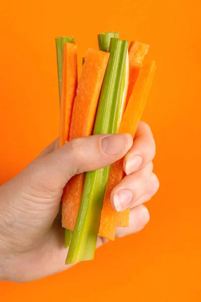 Fresh carrots and celery sticks in woman\'s hand on bright colorful background. Healthy food concept. Copy space