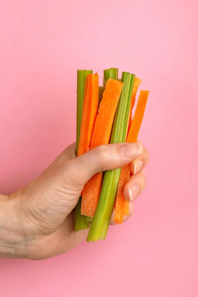 Fresh carrots and celery sticks in woman's hand on bright colorful background. Healthy food concept. Copy space