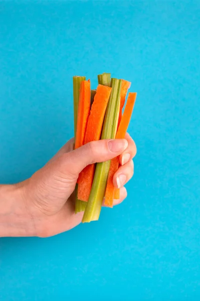 Fresh carrots and celery sticks in woman\'s hand on bright colorful background. Healthy food concept. Copy space