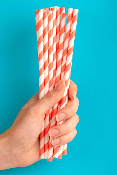 Woman is holding red and white paper straws in hand on bright background. Event and party supplies. Earth pollution concept. Copy space