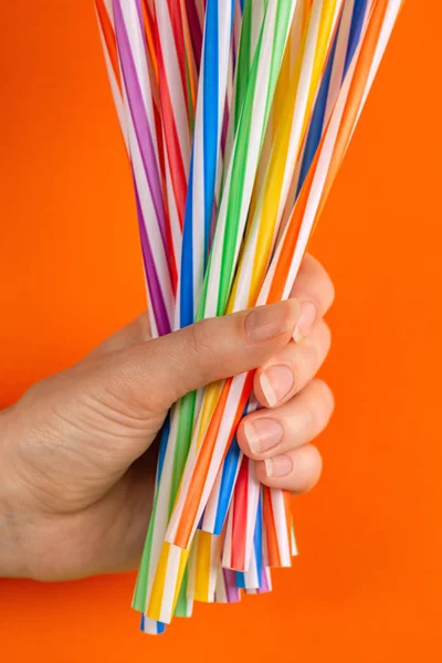 Woman is holding colorful plastic straws in hand on bright background. Event and party supplies. Earth pollution concept