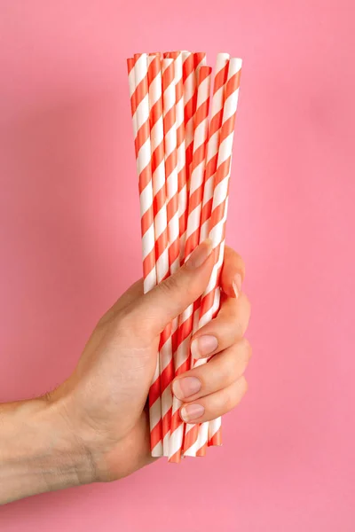 Woman is holding red and white paper straws in hand on bright background. Event and party supplies. Earth pollution concept. Copy space