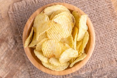 Çıtır patates cipsi çuval bezi peçete üzerinde ahşap kase oluklu. Ahşap arka plan. Abur cubur. Kopya alanı