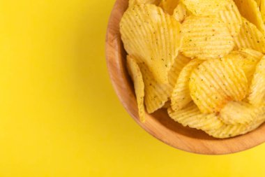 Çıtır patates cipsi ahşap kase parlak sarı zemin üzerine oluklu. Abur cubur. Kopya alanı