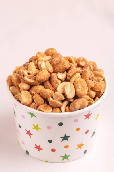 Roasted peanuts in paper cup on light marble background. Movie snacks. Copy space