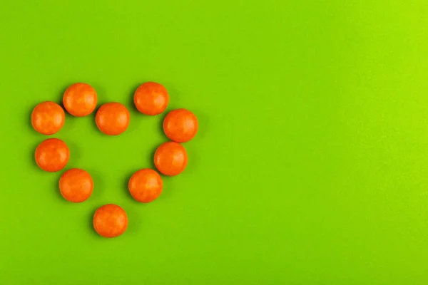 Smalto Ricoperto Cioccolato Caramelle Arancioni Forma Cuore Sfondo Verde Brillante — Foto Stock