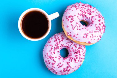 Serpin ve parlak mavi zemin üzerine koyu kahve fincan ile iki lezzetli leylak donut. Sağlıksız, ama lezzetli tatlılar. Uzay kopyalayın. Üstten görünüm