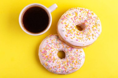 Serpin ve parlak sarı zemin üzerine kahve ile iki lezzetli vanilyalı donut. Sağlıksız, ama lezzetli tatlılar. Uzay kopyalayın. Üstten görünüm