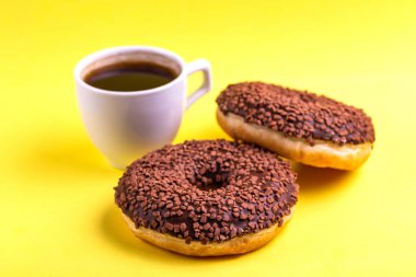 Serpin ve parlak sarı zemin üzerine kahve ile iki lezzetli çikolatalı çörek. Sağlıksız, ama lezzetli tatlılar. Uzay kopyalayın. Yatay görünüm