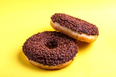 İki lezzetli çikolatalı çörek ile parlak sarı zemin üzerine serpin. Sağlıksız, ama lezzetli tatlılar. Uzay kopyalayın. Yatay görünüm